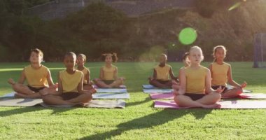 Çeşitli okul çocukları yoga dersleri sırasında minderlerin üzerinde oturup meditasyon yapıyorlar. İlkokuldaki çocuklar yazın.