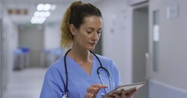 Düşünceli beyaz kadın sağlık çalışanı hastanenin koridorunda dijital tablet kullanıyor. Sağlık ve Tıp Konsepti