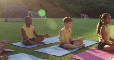 Çeşitli okul çocukları yoga dersleri sırasında minderlerin üzerinde oturup meditasyon yapıyorlar. İlkokuldaki çocuklar yazın.