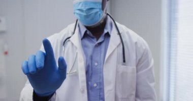 Yüz maskesi ve ameliyat eldiveni takan Afrikalı Amerikalı erkek doktorların orta kesimi. Coronavirus covid 19 salgını sırasında ilaç, sağlık ve sağlık hizmetleri.