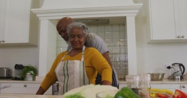 Afrika kökenli Amerikalı son sınıf öğrencisi evdeki mutfakta karısına önlük bağlıyor. emekli çift yaşam tarzı konsepti