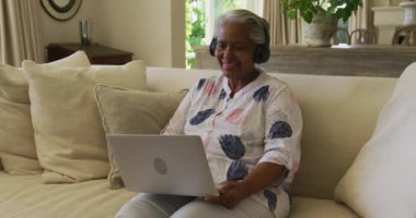 Evde dizüstü bilgisayarında video görüşmesi yaparken kulaklık takan Afrikalı Amerikalı son sınıf öğrencisi bir kadın. emeklilik son sınıf yaşam tarzı konsepti