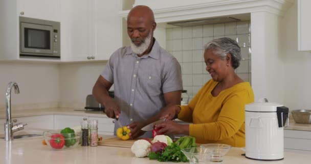 アフリカ系アメリカ人の先輩夫婦が自宅のキッチンで野菜を切り刻む 定年退職したシニアカップルのライフスタイルのコンセプト — ストック動画