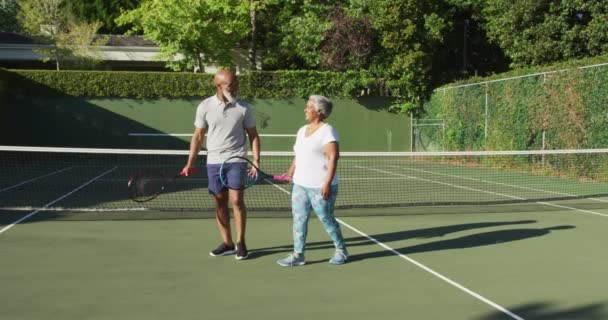 アフリカ系アメリカ人のシニアカップルがテニスコートで互いに話し合うラケットを持っています 引退スポーツやアクティブなシニアライフスタイル — ストック動画