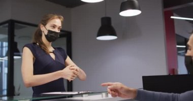 Yüz maskeli beyaz kadın ofis resepsiyonunda el ve tabelaları dezenfekte ediyor. Coronavirus covid 19 salgını sırasında modern bir ofiste bağımsız bir iş..