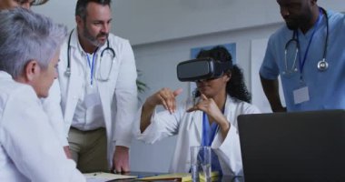 Masadaki Asyalı kadın doktor, etrafında bir grup meslektaşın toplandığı VR kulaklığı kullanıyor. ilaç, sağlık ve sağlık hizmetleri.