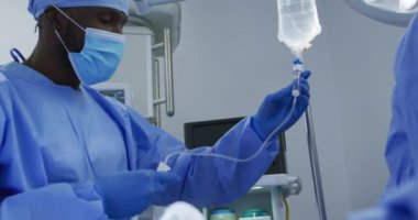 Afrika kökenli Amerikalı erkek cerrah koruyucu giysiler giyip ameliyathanede serumu hazırlıyor. Coronavirus covid 19 salgını sırasında ilaç, sağlık ve sağlık hizmetleri.