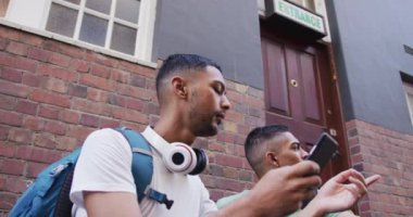 İki melez erkek arkadaş sokakta oturuyor, konuşuyor ve akıllı telefon kullanıyor. Sırt çantalı tatil şehir seyahati.