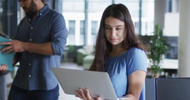 Beyaz iş kadınının portresi ofiste dizüstü bilgisayar kullanarak kameraya bakıp gülümsüyor. Modern bir ofiste bağımsız yaratıcı iş.