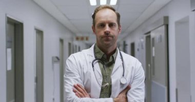Hastanenin koridorunda kollarını kavuşturmuş beyaz erkek doktorun portresi. Sağlık ve Tıp Konsepti