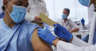 Karışık ırk doktoru, erkek meslektaşlarına kovid aşısı yapıyor. İkisi de maske takıyor. covid 19 koronavirüs salgını sırasında ilaç, sağlık ve sağlık hizmetleri.