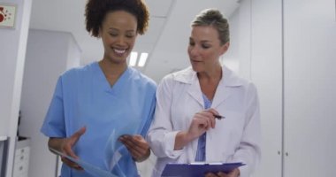 Diverse female doctor and medical worker standing in hospital corridor and talking. medicine, health and healthcare services.