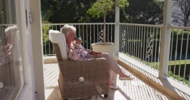 Kafkasyalı son sınıf öğrencisi kadın evdeki balkonda bir sandalyede otururken kahve içiyor. emeklilik son sınıf yaşam tarzı konsepti