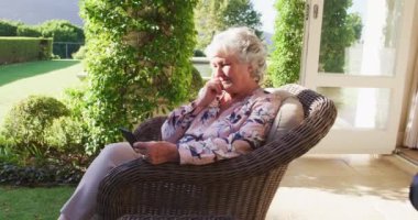 Açık havada sandalyede otururken akıllı telefon kullanan düşünceli, beyaz bir kadın. emeklilik son sınıf yaşam tarzı konsepti