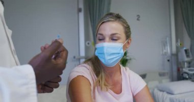 Yüz maskesi takan beyaz kadın hasta hastane yatağında iğneyi bekliyor. Coronavirus covid 19 salgını sırasında ilaç, sağlık ve sağlık hizmetleri.