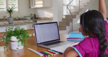 Masada oturan İspanyol kız kulaklık takıyor ve dizüstü bilgisayar kullanıyor. Karantina süresince evde tecrit altında..