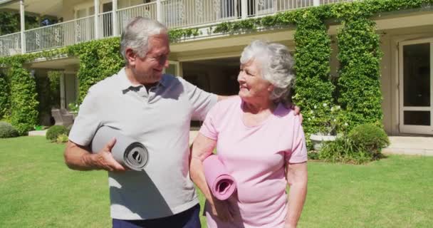 幸せな白人のシニアカップルは 太陽の下で庭でヨガマットを運んで歩くことを受け入れ運動をします 隔離中に隔離された家で — ストック動画