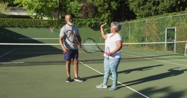 アフリカ系アメリカ人のシニアカップルがテニスコートで互いに５つのラケットを持っている 引退スポーツやアクティブなシニアライフスタイル — ストック動画