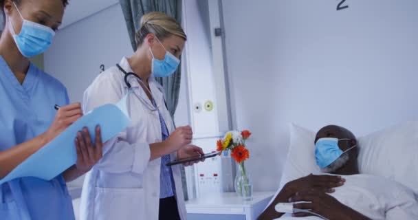 不同的女医生在医院病床上与男病人交谈时都戴着口罩 Coronavirus Covid大流行病期间的医疗 保健和保健服务 — 图库视频影像