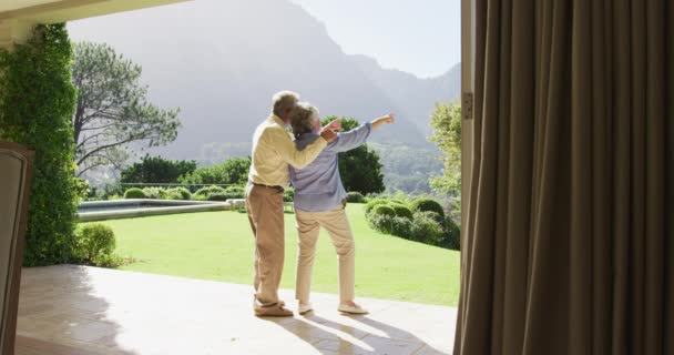 庭の近くに立って演出を指している白人の高齢者のカップルの背面ビュー 定年退職したシニアカップルのライフスタイルのコンセプト — ストック動画