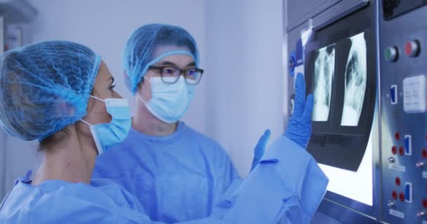 外科用キャップとフェイスマスクを着用した多様な男性と女性の外科医がX線を議論する コロナウイルスの19大流行時の医療 医療サービス — ストック動画