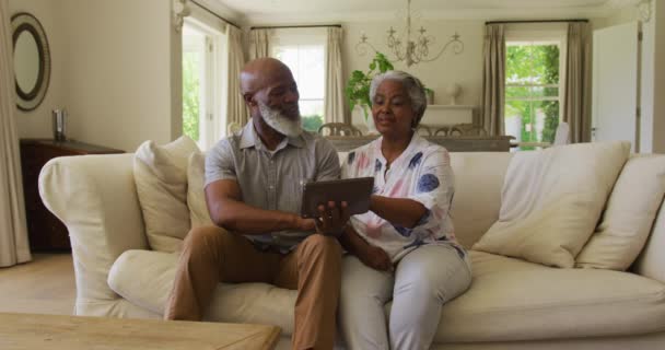 アフリカ系アメリカ人のシニアカップルは 自宅でデジタルタブレットを使用しながら お互いを見て笑っています 定年退職したシニアカップルのライフスタイルのコンセプト — ストック動画