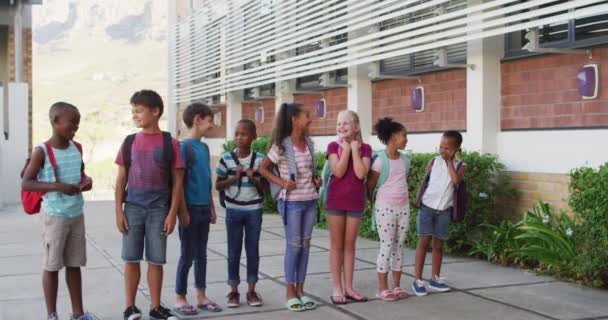 Diverso Grupo Escolares Con Mochilas Sonriendo Parados Fila Patio Escuela — Vídeo de stock