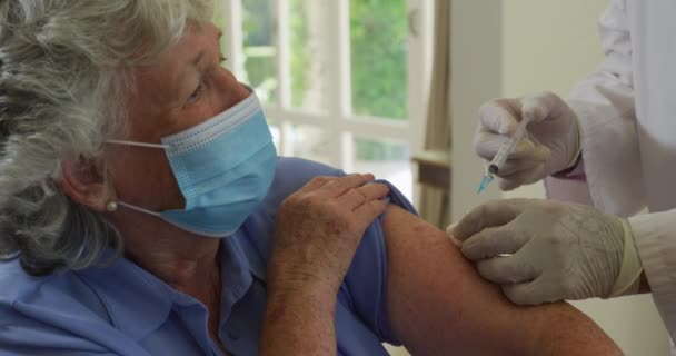 白人のシニア男性医師がフェイスマスクを着用し 自宅のシニア女性にCovid 19ワクチンを注射する コロナウイルス発生防止のための予防接種 — ストック動画