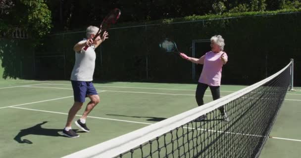 ゲームをプレイした後 太陽の下で屋外テニスコートに抱擁幸せな白人のシニアカップル 現役引退生活スポーツ趣味 — ストック動画
