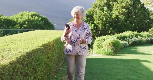 園内を歩いていると スマホで話していると笑顔になる白人の先輩女性 定年退職者のライフスタイルコンセプト — ストック動画