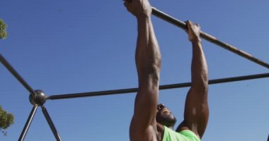 Dışarıda egzersiz yapan, tırmanma iskeletinde barfiks çeken formda Afro-Amerikan bir adam. Spor sahasında spor eğitimi için çapraz eğitim.