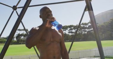 Formda olmayan Afro-Amerikan bir adam dışarıda kareye tırmanıyor, dinleniyor ve su içiyor. Spor sahasında spor eğitimi için çapraz eğitim.