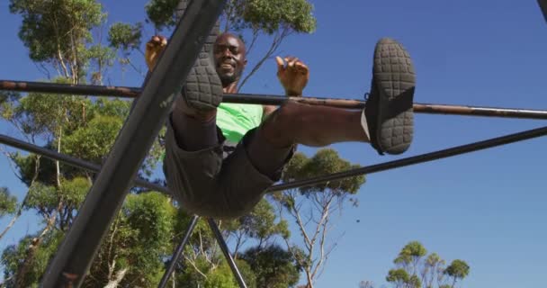 外で運動するアフリカ系アメリカ人の男にフィットし 登山フレームの上にハンギングプルアップを行います スポーツ分野でのフィットネスのためのクロストレーニング — ストック動画