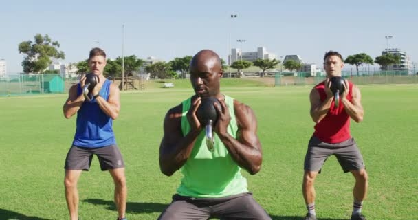 一组有三个健康的男人 他们在室外锻炼 蹲着举重水壶 在运动场上为健身进行交叉训练 — 图库视频影像
