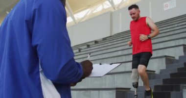 Çeşitli erkek antrenörler ve protez bacak eğitimi almış engelli bir sporcu merdivenlerden aşağı koşuyor. Spor stadyumunda profesyonel atlet eğitimi.