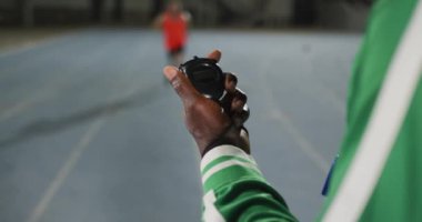 Afrika kökenli Amerikalı erkek koçun eli, koşu bıçağıyla engelli erkek sporcunun zamanını kontrol ediyor. Spor stadyumunda profesyonel atlet eğitimi.