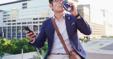 Asyalı adam kahve içiyor ve şirket parkının çatısında otururken akıllı telefon kullanıyor. iş ve yaşam tarzı kavramı