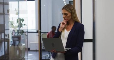 Modern ofiste dikilirken dizüstü bilgisayar kullanan gülümseyen beyaz kadın. iş, profesyonellik ve ofis kavramı