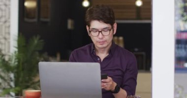 Bilgisayarlı Asyalı bir adam kafede otururken akıllı telefondan konuşuyor. iş ve yaşam tarzı kavramı