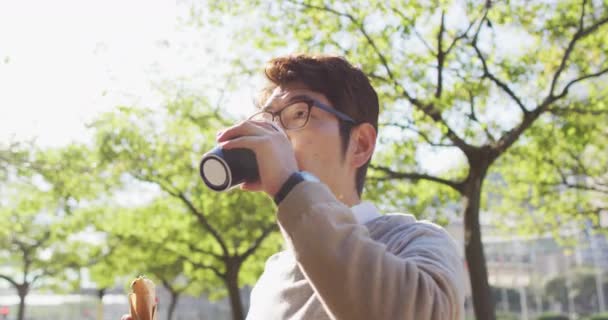 アジア系の男性は屋外でコーヒーを飲みながら軽食をとります ビジネスやライフスタイルの概念 — ストック動画