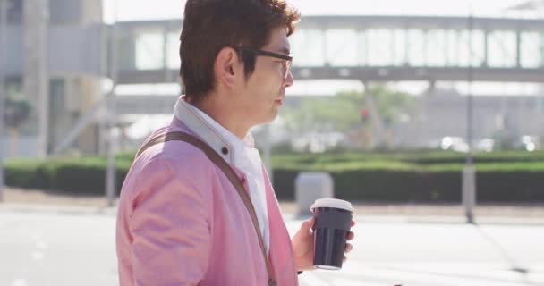 通りを歩いていると アジア人の男性がコーヒーを飲み スマートフォンを使っています ビジネスやライフスタイルの概念 — ストック動画