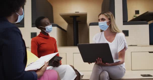 オフィスでは3人の多様な女性のオフィスの同僚が顔のマスクを着用して話し合っている コロナウイルスの職場での衛生と社会的距離は19のパンデミックを克服しました — ストック動画