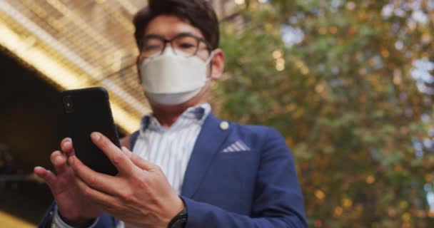 Aziatische Man Draagt Gezichtsmasker Met Behulp Van Smartphone Terwijl Hij — Stockvideo