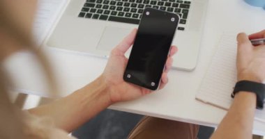 Beyaz iş kadını masasında oturuyor, akıllı telefon kullanıyor ve notlar alıyor. Modern bir ofiste bağımsız yaratıcı iş.