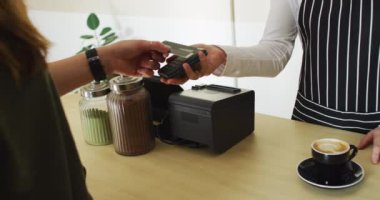 Kafkasyalı garson temas kurmadan ödeme alıyor ve beyaz kadın müşteriye kahve kupası veriyor. Küçük bağımsız kafe işletmesi.