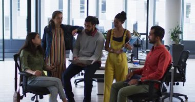 Dizüstü bilgisayar, tablet ve belgelerle kameraya gülümseyen çeşitli iş arkadaşları. Bağımsız yaratıcı bir şirkette çalışmak..