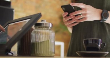 Beyaz kadın müşteri akıllı telefon tutuyor ve tezgahtan bir fincan kahve alıyor. Küçük bağımsız kafe işletmesi.