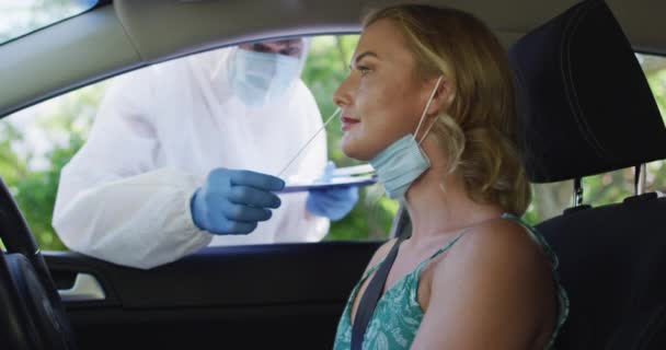 白人女性は車の中で 顔のマスクを着用し 屋外で医療従事者によって行われた鮮やかなテストを受けて座っている コロナウイルスの健康診断と予防策 Covid 19パンデミック — ストック動画