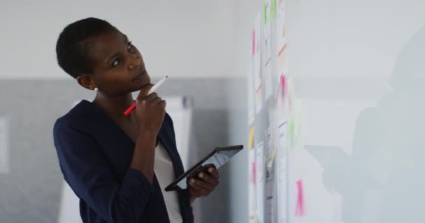 アフリカ系アメリカ人の実業家はホワイトボードで考え メモを取る 現代のオフィスで独立した創造的なビジネスを — ストック動画