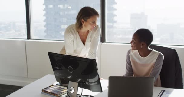 2人の多様な女性同僚がラップトップを見てオフィスで議論しています 現代のオフィスで独立した創造的なビジネスを — ストック動画